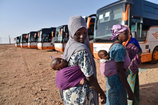 Des migrants nigériens en Algérie attendent à côté des bus alors qu'ils sont rapatriés par les autorités algériennes au Niger le 29 juin 2018, à Laghouat, dans le nord de l'Algérie.