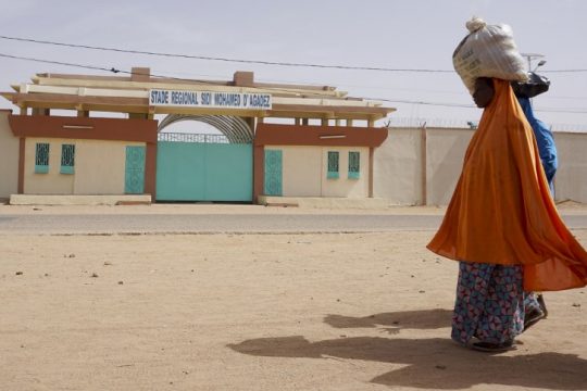 Des femmes portent des sacs sur la tête en passant devant le stade Sidi Mohamed à Agadez, au nord du Niger